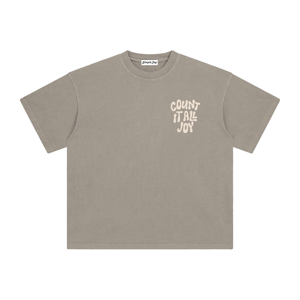 A taupe gray short-sleeve t-shirt with a cream-colored graphic text print reading 'COUNT IT ALL JOY' on the left chest, displayed flat against a solid white background.